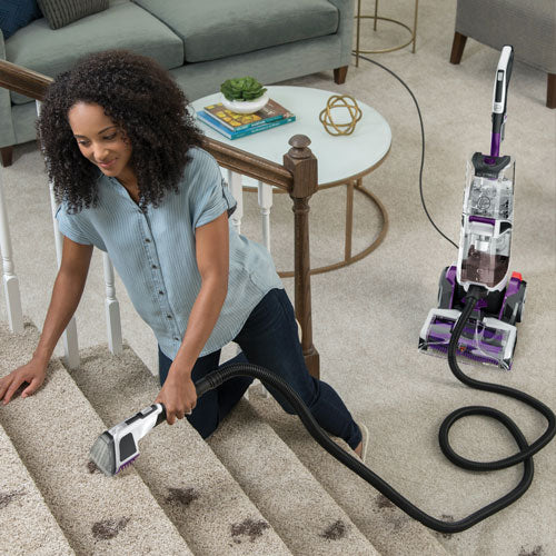 A woman uses the antimicrobial pet tool to clean carpet on stairs